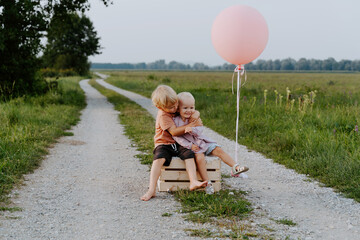Brother and sister sitting together on wooden box in countryside. Happy siblings in nature....