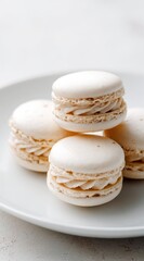 Delicate, pale-cream macarons stacked on a white plate