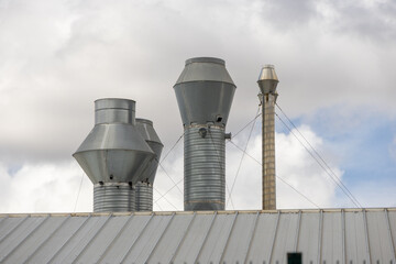 Obraz premium Industrial exhaust pipes rising from metal roof into cloudy sky