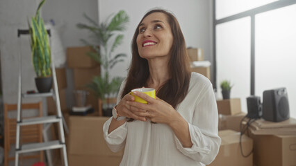 Woman enjoying coffee surrounded by moving boxes in cozy new home filled with plants and furniture exploring fresh beginnings with a warm and cheerful smile indoors.