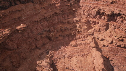 Majestic layers of red rock tower over a deep canyon, illuminated by the bright midday sun.