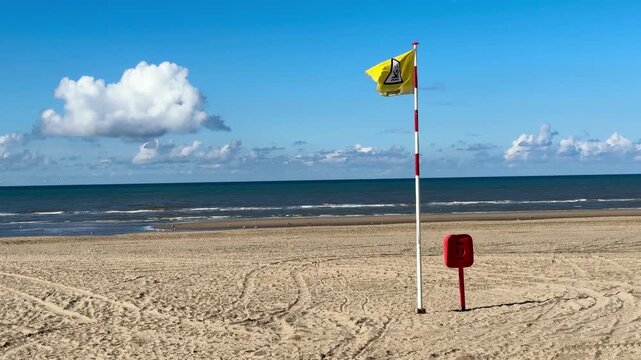 Beach landscape with a yellow flag waving in the wind outdoor at daytime along the coast warning for swimming in the North Sea without people in Zandvoort in The Netherlands.