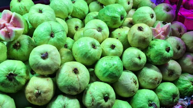 Both green and ripe red guavas are available for sale at a shop, showing a variety of fresh fruit options.