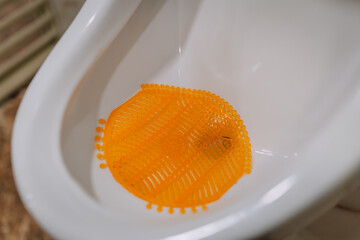 Close-up of a white urinal with an orange urinal screen inside, typically used for hygiene and odor control in public or commercial restrooms.