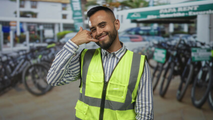 Man in high visibility vest with hand to ear for call on street by bike rental parking; friendly service.