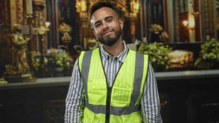 Young hispanic man in reflective safety vest placing hand on chest in a church building; faith...