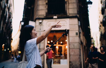 Asian woman with long dark hair talks to camera on smartphone stabilizer while walking down street, creating engaging vertical video content for social media or vlog audience.