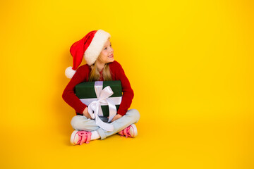 Playful christmas girl with santa hat holding gift against bright yellow background