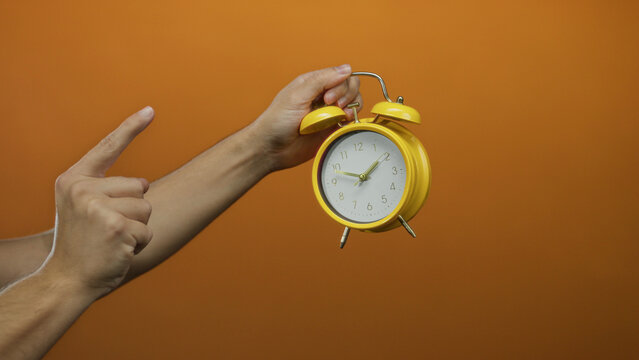 Man hand holding yellow clock against orange wall vividly showing time management emphasis.