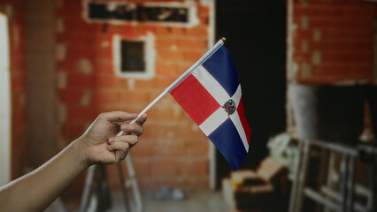 Hand holding dominican republic flag indoors on construction site, symbolizing national pride with...