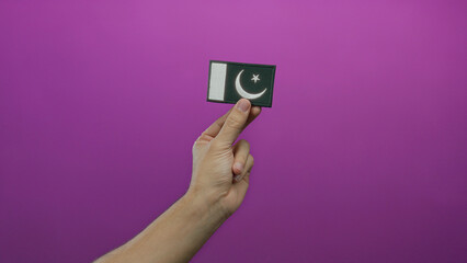 Man hand holding pakistan flag embroidery on pink background representing national pride and identity with a clear isolated setting for cultural significance and design.