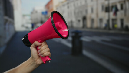 Man holding pink megaphone on city street suggests urban protest or announcement, highlighting civic engagement and public communication in a bustling outdoor setting.