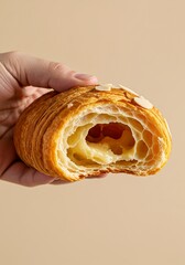 Golden croissant with almond filling held in hand, pastel beige background, breakfast photography for indulgent food styling and gourmet branding