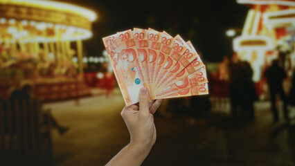 Man holding philippine pesos in hand, set against the lively backdrop of a vibrant outdoor carnival, showcasing the dynamic atmosphere of fun and commerce under colorful lights.