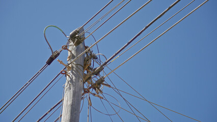 Wooden pole wired with electricity cables under a clear blue sky in a sunny outdoor setting, showcasing an essential infrastructure element in a rural environment.