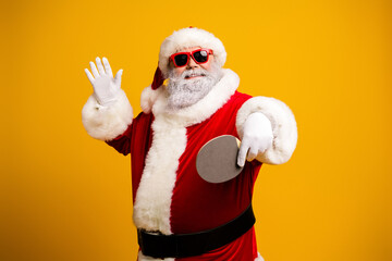Santa Claus in festive attire plays table tennis with a joyful gesture on vivid yellow background