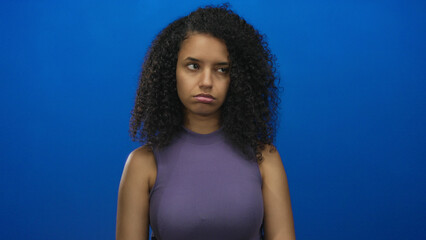 Hispanic woman wearing purple sleeveless top slumps bare shoulders in studio facing blue wall;...