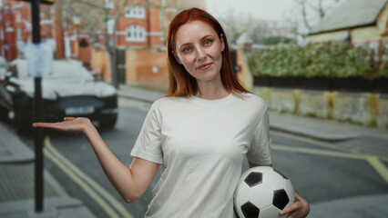 Woman smiling holding soccer ball on urban street with red hair showcasing beauty in casual white shirt outdoors during daylight