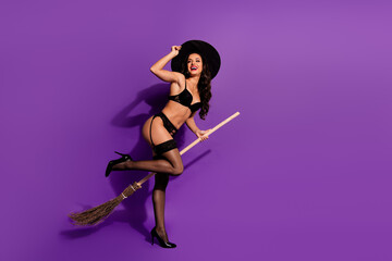 Sensual Halloween witch in lingerie with hat and broomstick on vibrant purple background, enjoying...