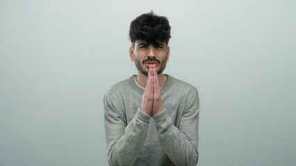Young man in gray sweater poses against simple white background in thoughtful prayerful gesture expressing hope and contemplation.