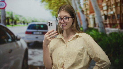 Fototapeta premium Woman holding smartphone points finger to phone screen on sunlit city street in front of building; confidence.