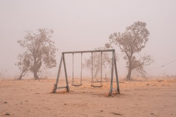 Empty playground swings in a dusty, hazy landscape