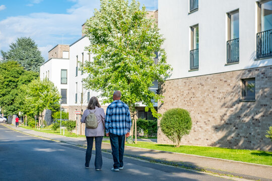 Happy Active mature couple walking hand in hand along urban street, suburban neighborhood, elderly man and woman spending time together around residential, apartment buildings, modern architecture