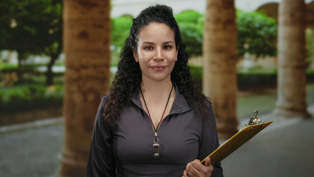 Woman wearing whistle holding clipboard in outdoor park setting with stone pillars and lush greenery providing a tranquil background for this scene. - Powered by Adobe