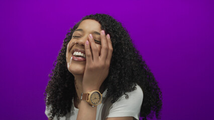 African american woman with hand on cheek laughing in purple studio wearing white t shirt;...