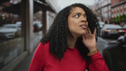 Woman cups her ear and tilts head while straining to hear passing traffic on a busy city street;...