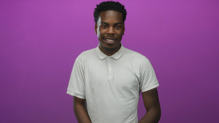 Man in white polo shirt standing in purple studio smiling with relaxed posture and direct gaze;...