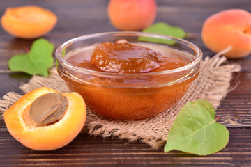 Apricot jam in a small bowl and fresh apricots on the table. Close-up.
