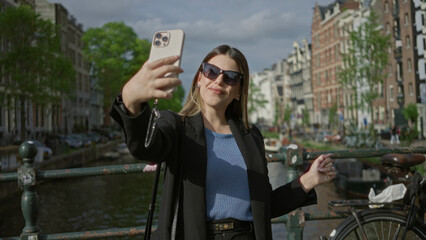 Woman enjoying canals with smartphone in sunny amsterdam, wearing sunglasses and capturing moments.