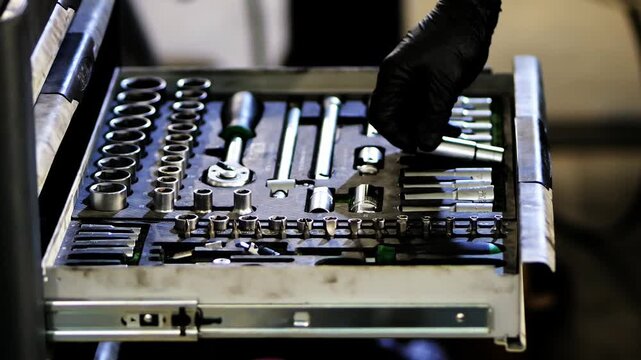Detail video in auto repair shop with selective focus, showing mechanic hands putting socket wrench into toolbox drawer with complete socket set.