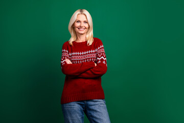 Smiling woman in festive sweater posing confidently with arms crossed on a green background for a holiday celebration