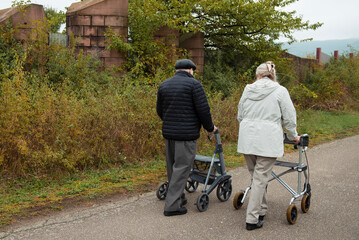 Elderly people taking a walk with help of walker with friends on a cold day through the park 