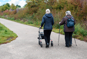 Elderly people taking a walk with help of walker with friends on a cold day through the park
