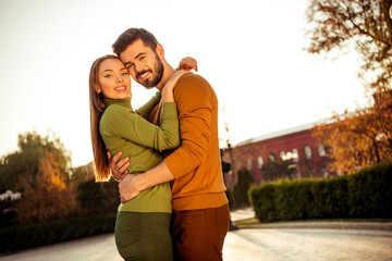 Obraz premium Happy couple embraces during an autumn walk through a sunlit park with vibrant foliage and a serene urban backdrop