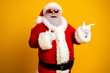 Festive Santa Claus Strikes a Cool Pose with Sunglass and a Cheerful Gesture Against a Vibrant Yellow Background