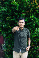 Serious man pointing finger in front of foliage