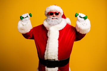 Santa Claus posing in festive attire with dumbbells, showcasing a humorous and trendy take on holiday fitness on a yellow backdrop