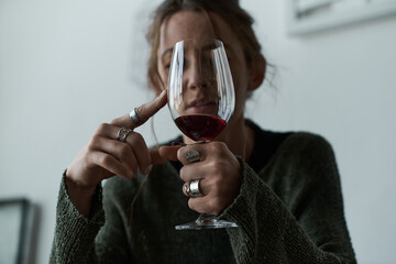 Young woman struggles with her feelings while observing wine at home in quiet reflection
