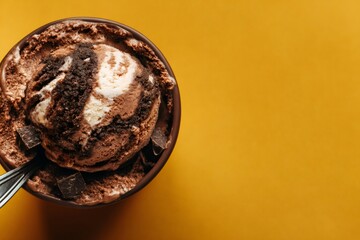 Chocolate cookie dough ice cream in a small bowl with a spoon and chocolate chips, shot from above on a yellow background