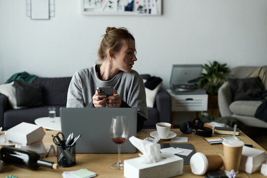 Young woman struggles with feelings of sadness while sitting at a cluttered desk in her home