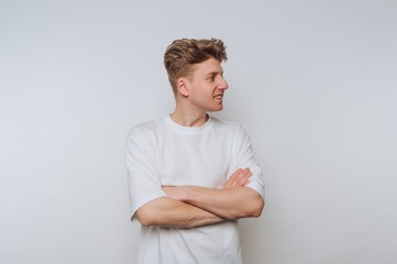Obraz premium Young man stands with arms crossed, smiling confidently against a plain white background in a casual setting