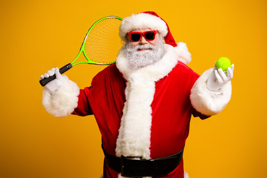 Santa Claus plays tennis wearing a fun costume featuring sunglass and holding a tennis ball on a vibrant yellow backdrop. - Powered by Adobe