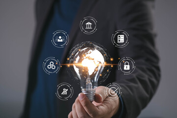 Businessman holding glowing light bulb with digital world map and business icons, symbolizing global business strategy, innovation, finance, cybersecurity, leadership, and digital transformation.