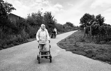 Elderly people taking a walk with help of walker with friends on a cold day through the park