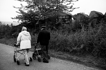 Elderly people taking a walk with help of walker with friends on a cold day through the park 