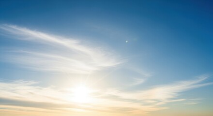 Obraz premium Serene sunset sky with wispy clouds and a bright sun peeking through, creating a tranquil atmosphere. Warm colors transition from yellow to orange as the day ends, offering a peaceful scene.